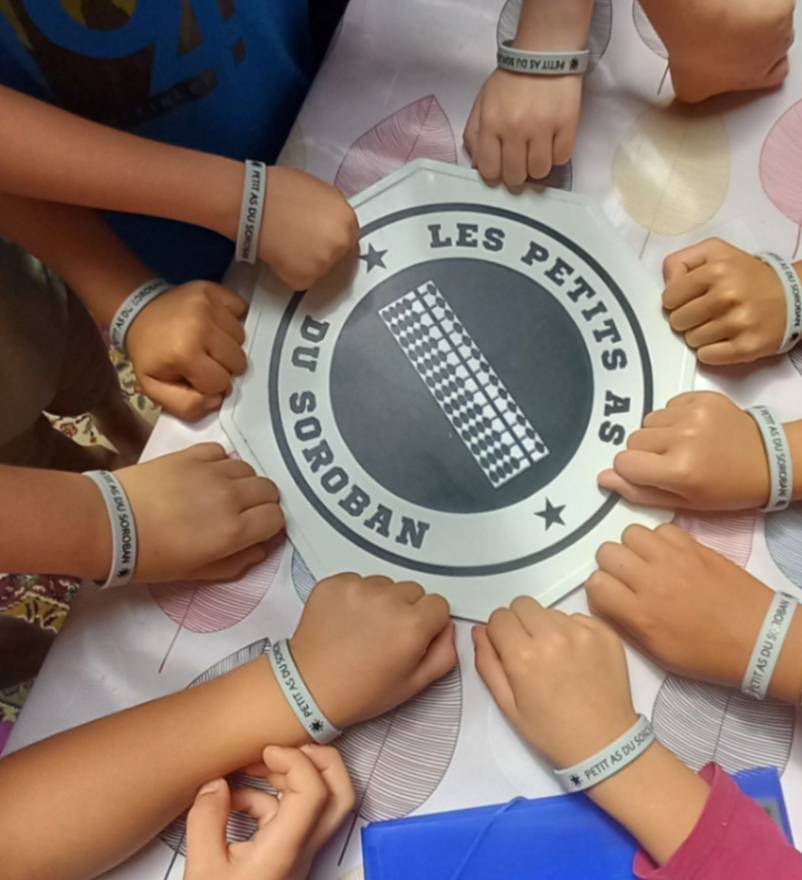 Enfants de l'Imaginarium (Donnezac- 33820 Gironde) arborant leur bracelet récompense autour du logo des petits as du soroban 